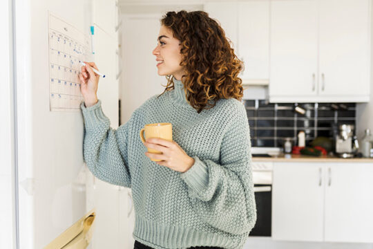 Woman marking her home calendar on refrigerator