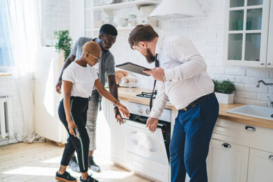 couple in kitchen with man inspecting oven