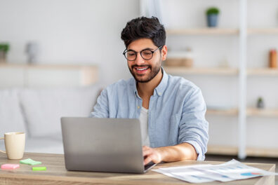 Young man working on laptop with reports on desk