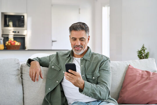 Mature man using his phone while sitting on couch