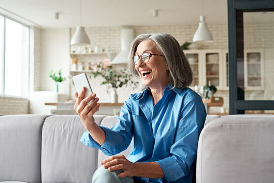 happy mature woman sitting on couch looking at mobile phone