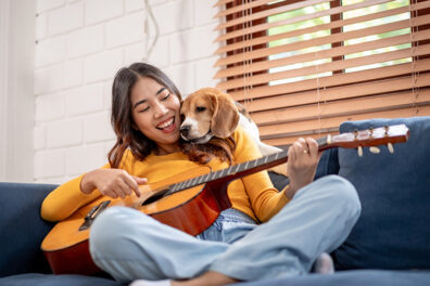 Young woman on couch playing guitar with her dog