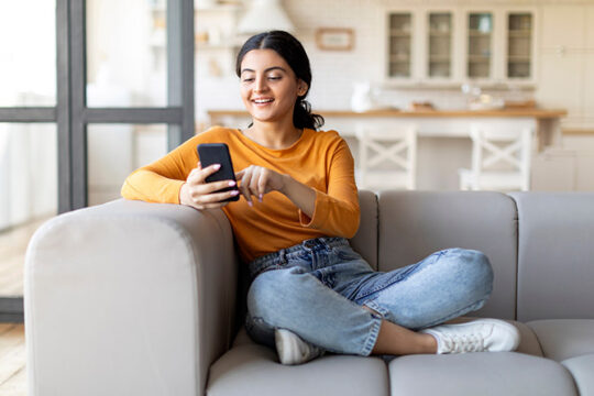 Young woman using her mobile phone while sitting on the couch