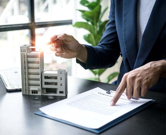 professional man standing near a model of an office building while pointing to a contract