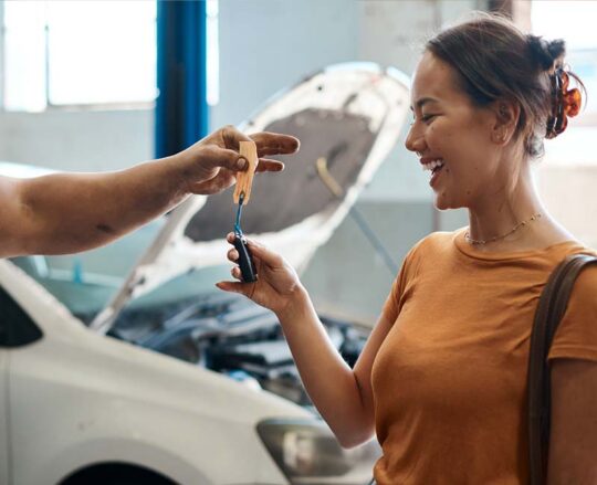 woman laughing as she is handed a car key from mechanic
