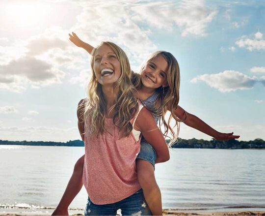 mom giving daughter a piggy back ride on the beach