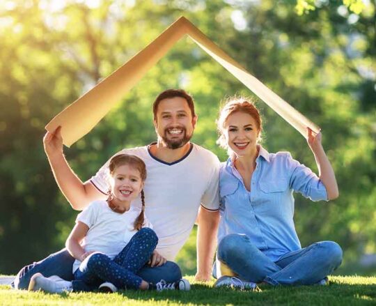 family sitting outside holding up cardboard roof