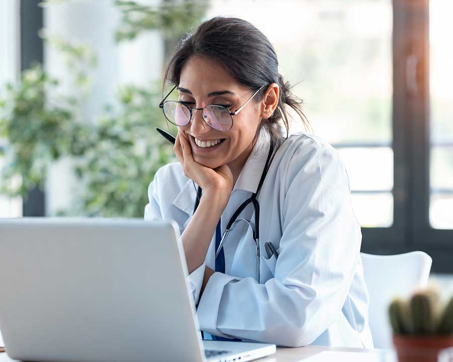 happy doctor sitting at desk with laptop