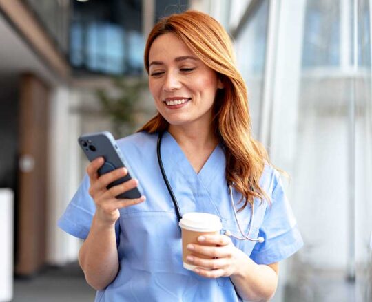 nurse standing with coffee and viewing mobile phone