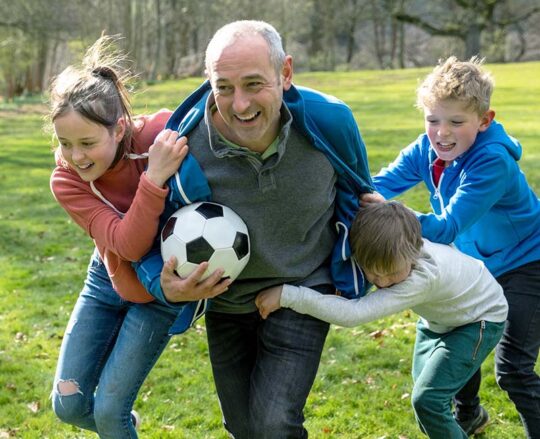 mature man playing soccer with children