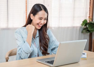 happy woman at laptop making yes gesture with fist